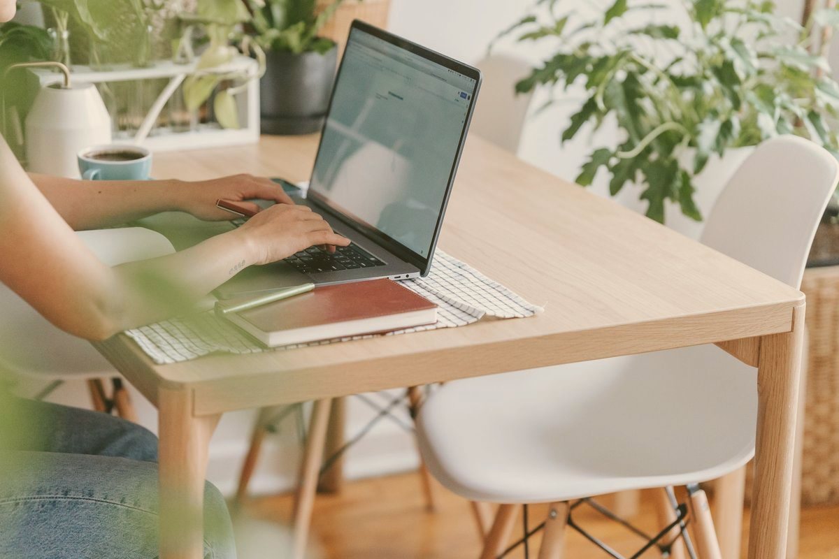 Laptop on a light wooden desk surrounded by houseplants