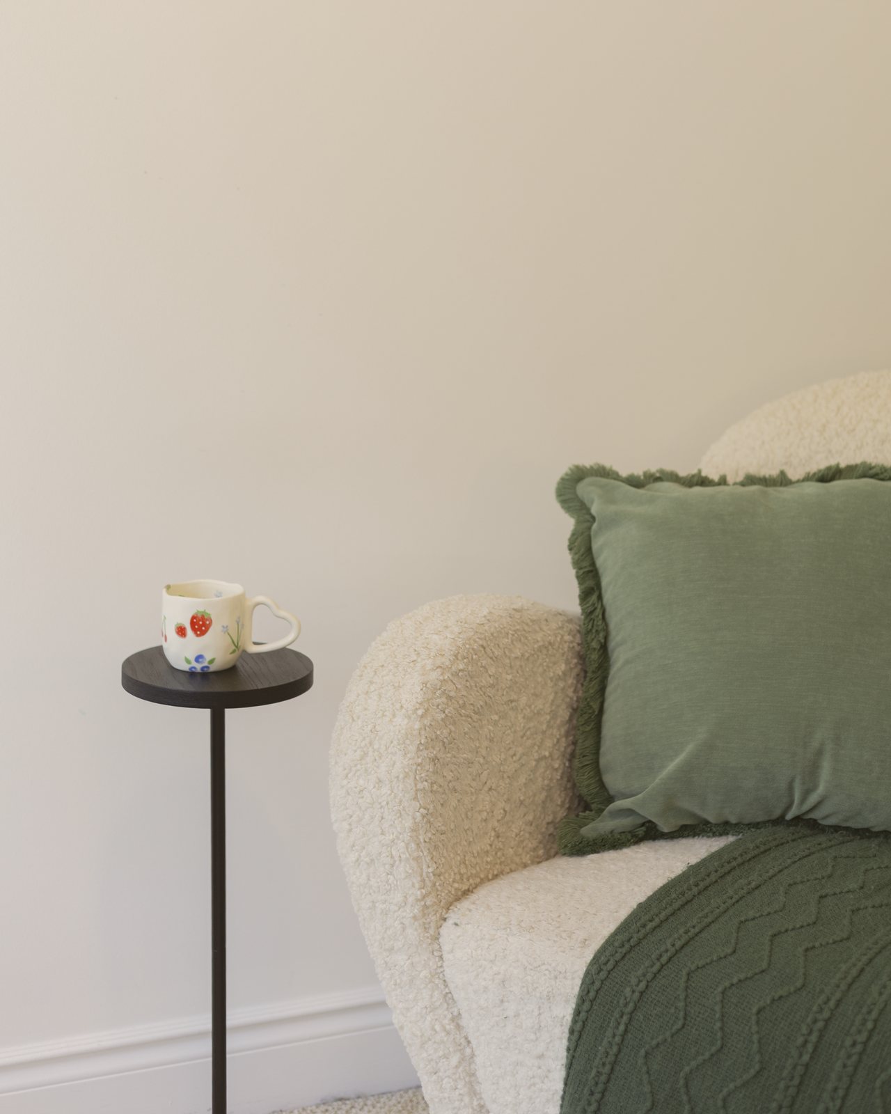 A cream armchair with a green pillow and throw beside a small table and mug in the Heart of Oak office