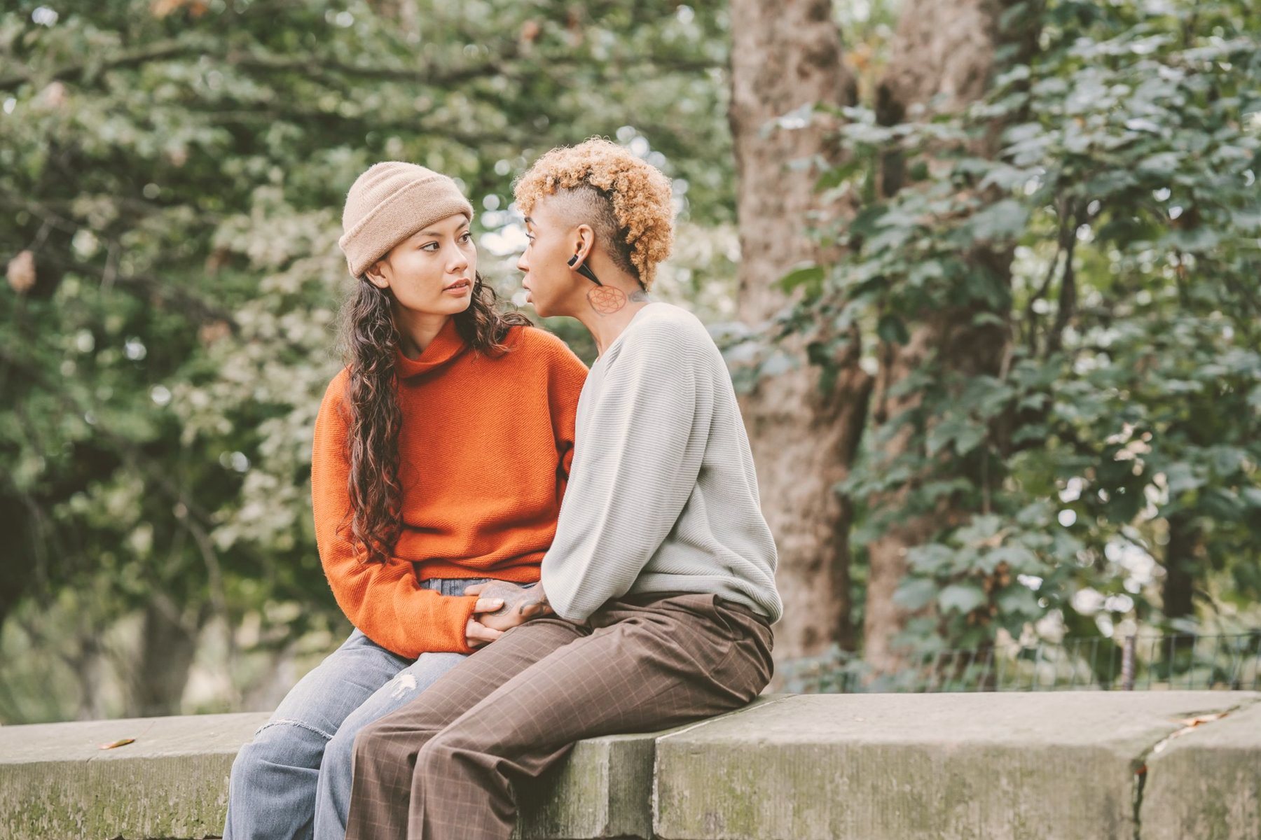 Two women sitting close and talking warmly in a green park, representing LGBTQIA+ affirming therapy in Oakville