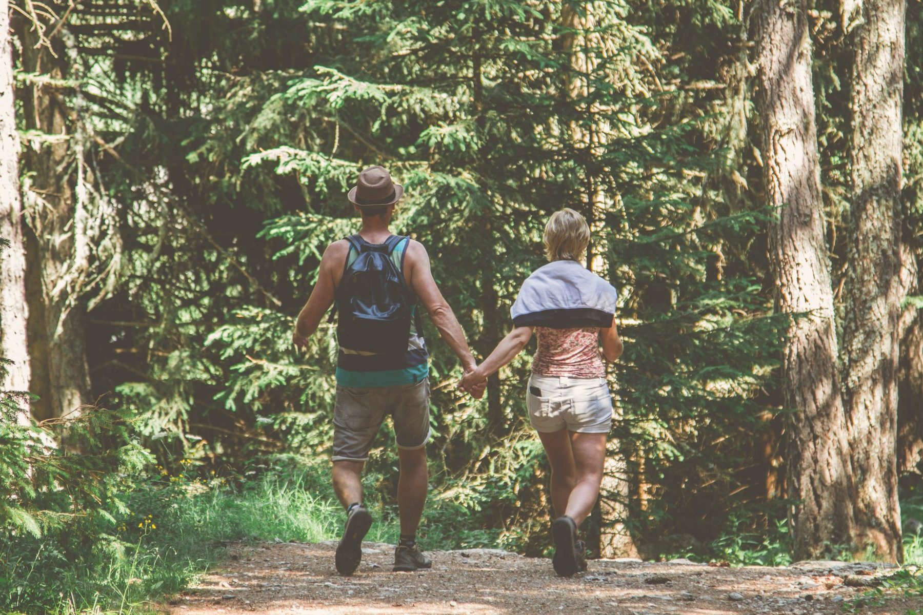 Couple holding hands walking a green forest trail, representing relationship and dating therapy